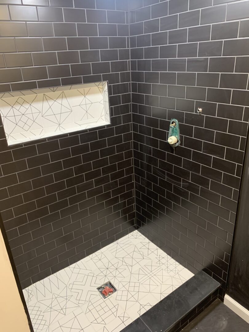 A black tiled shower with white tile and a black floor.