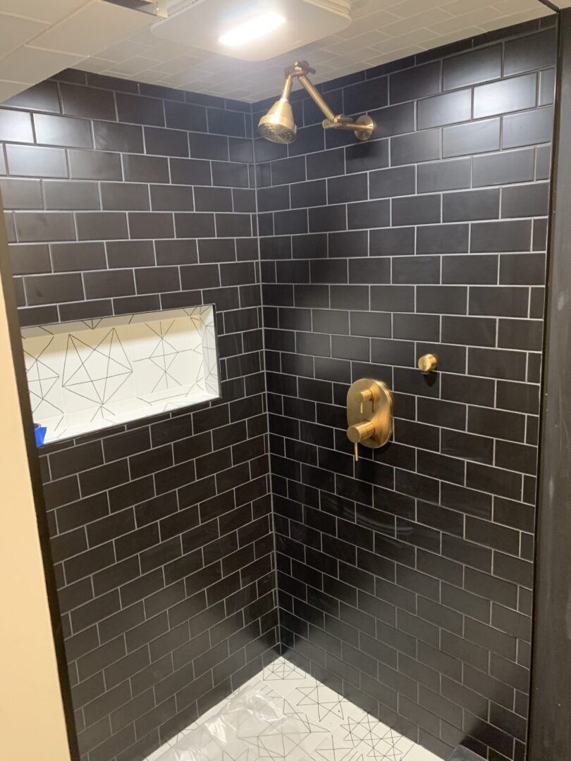 A black tiled shower with a gold faucet.