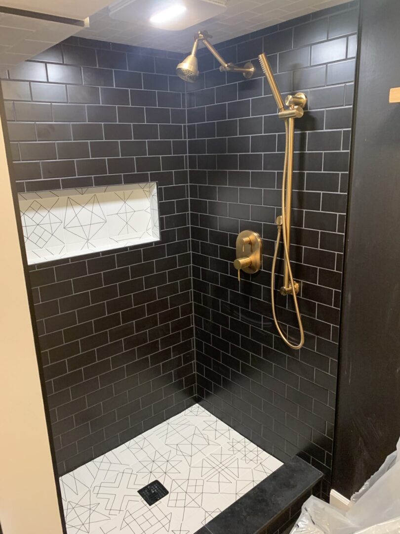 A black tiled shower with gold fixtures and white tile.